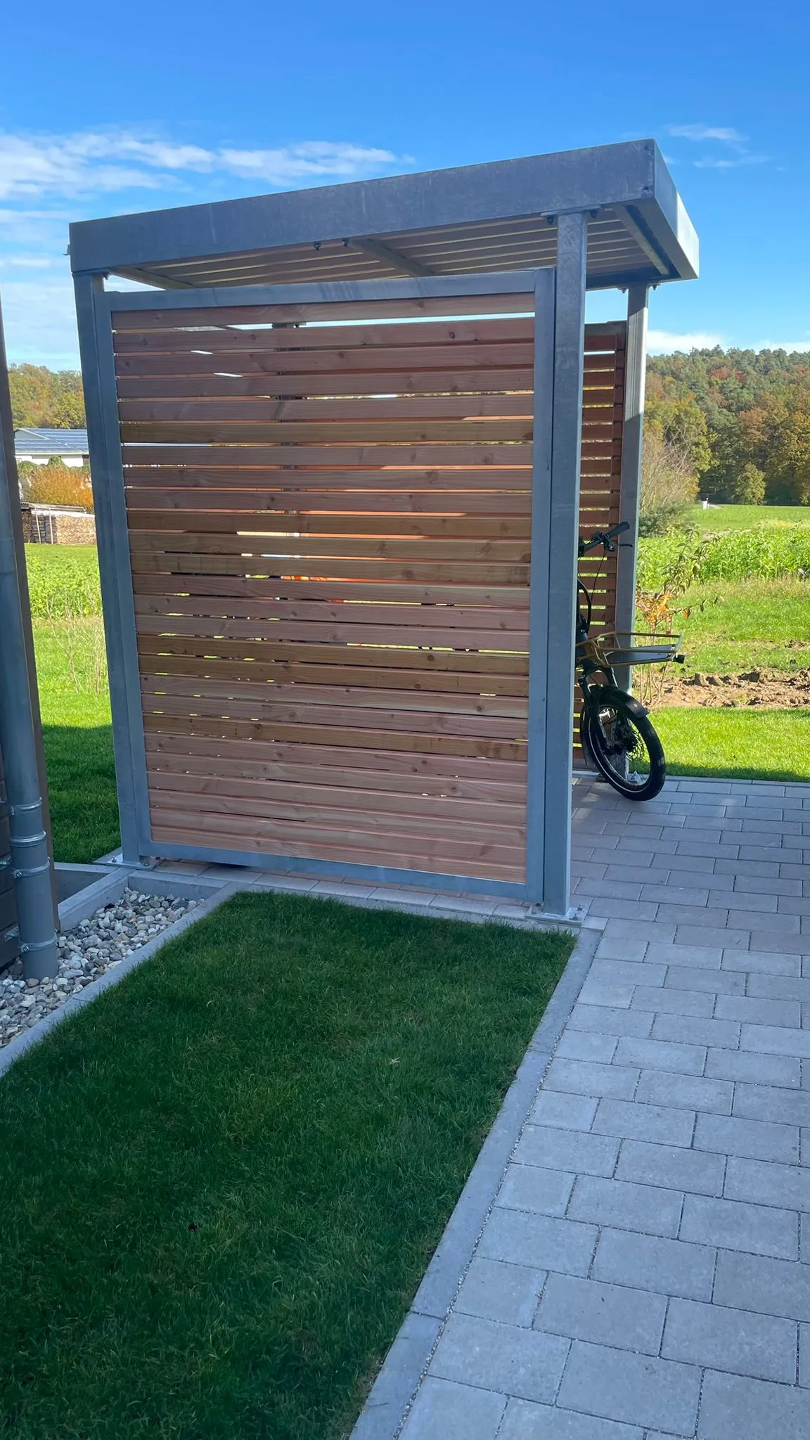 Frei stehender Fahrradunterstand mit Stahlrahmen und horizontaler Lärchenlattung am Feldrand