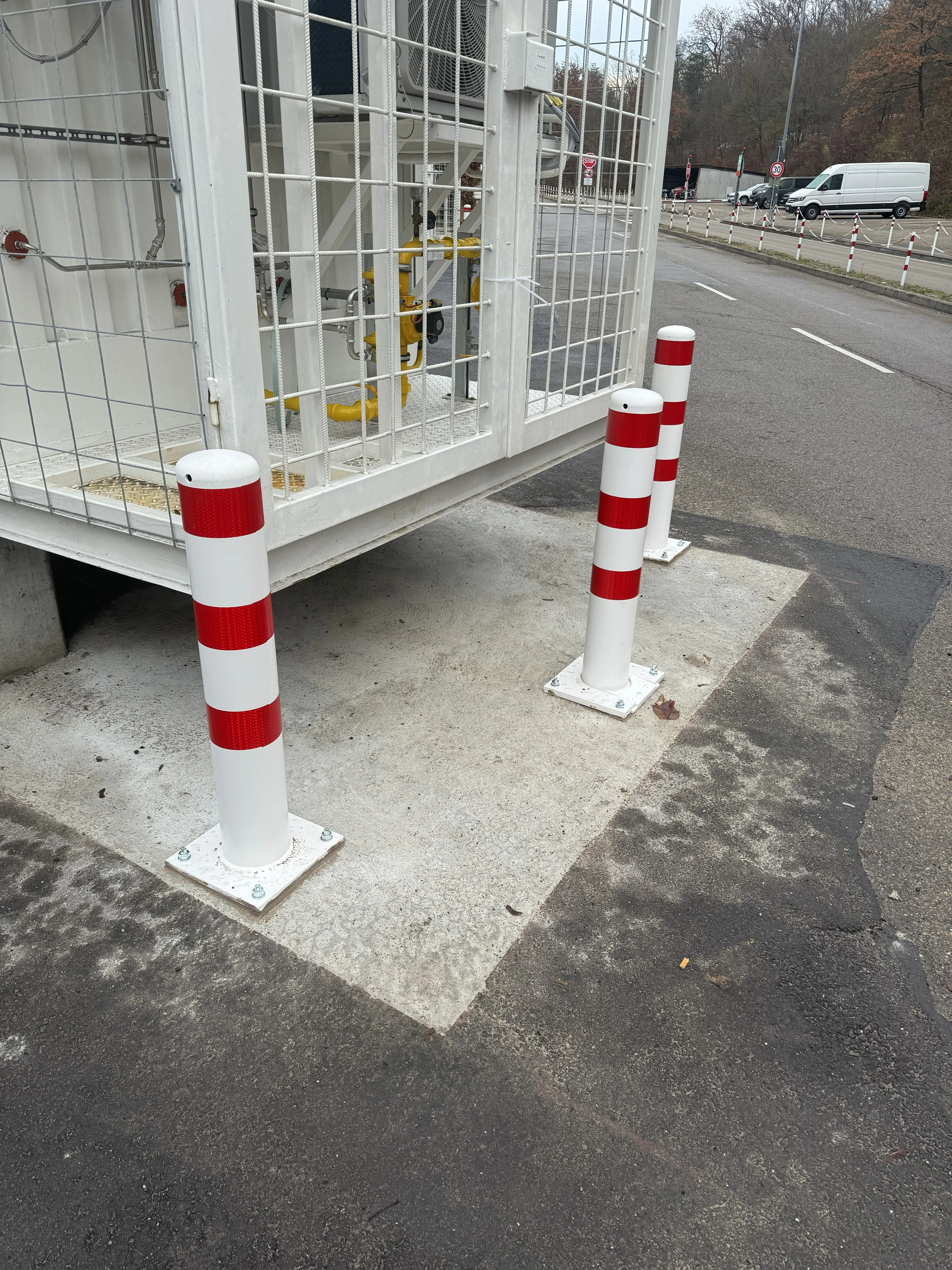 Weiß-rot lackierte Rammschutzpoller vor einer eingehausten Gasregelstation