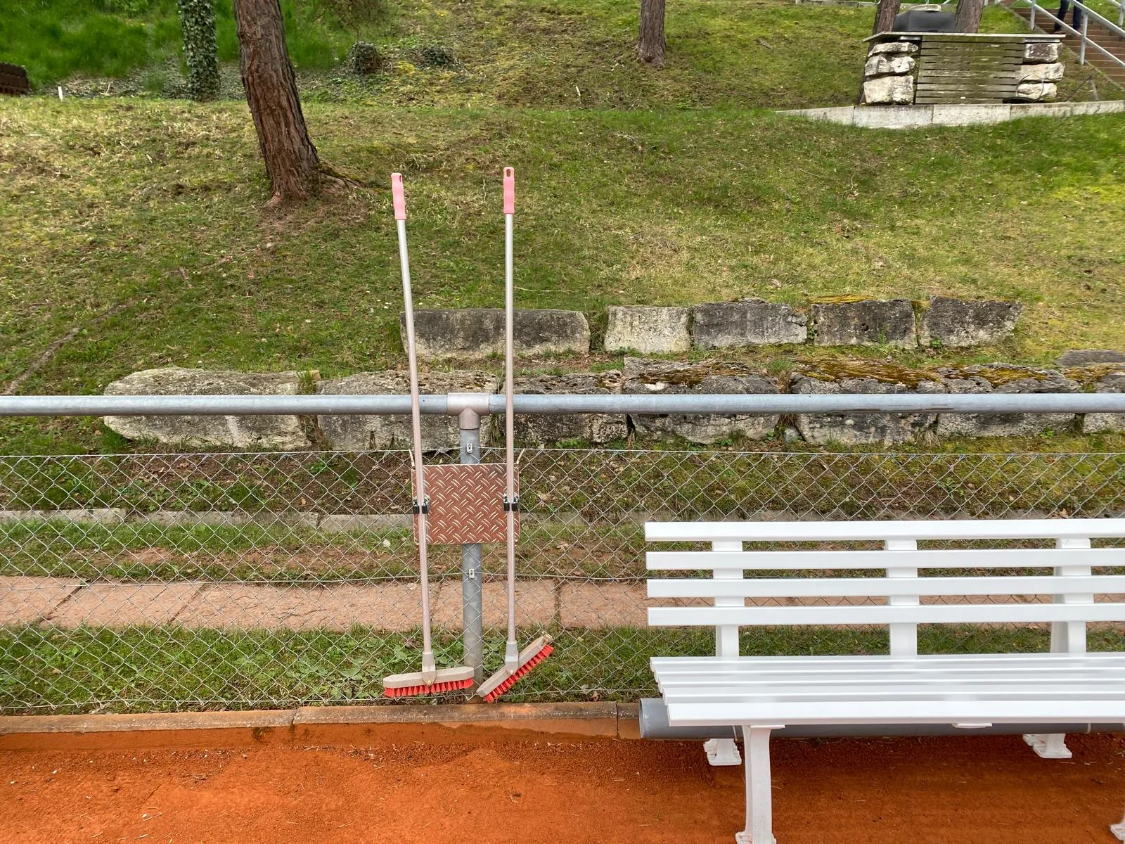 Eingebauter Besenhalter aus Aluminium-Riffelblech am Zaun eines Tennisplatzes