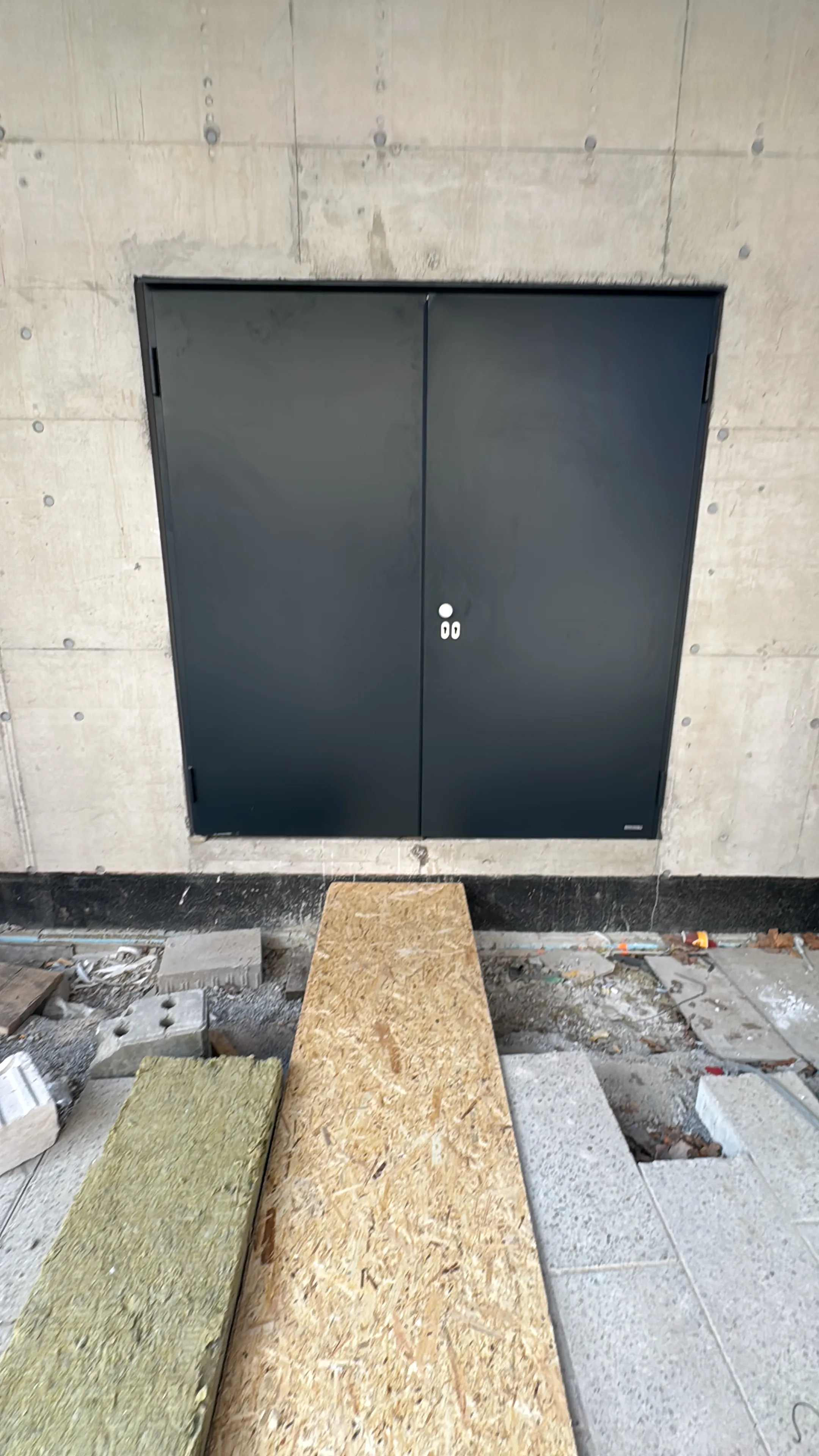 Zweiflügelige anthrazitfarbene Stahltür flächenbündig im Sichtbeton eines Traforaums